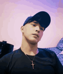 a young man wearing a hat and a cross necklace looks at the camera