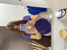 a woman in a purple shirt is taking a picture of herself in the mirror