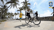 a woman is riding a bike on a sidewalk with a mascot in the background with the word brasil on it