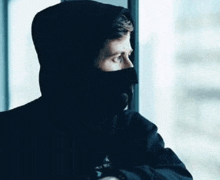 a man wearing a hoodie and a mask is looking out of a window .