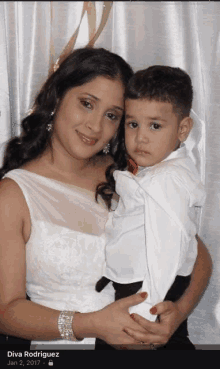 a woman in a white dress is holding a young boy in her arms