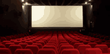 an empty movie theater with red seats and a large screen