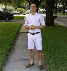 a young man wearing white shorts and a white shirt stands on a sidewalk