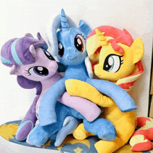 three stuffed ponies are hugging each other on a blanket