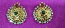 a pair of gold earrings with emeralds and rhinestones on a pink surface .