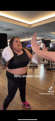 a woman wearing boxing gloves is giving a high five to another person in a gym .