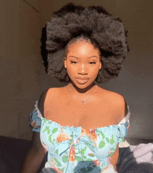 a woman with a big afro is sitting on a bed wearing a blue floral dress .