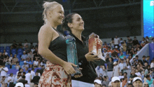 two women holding trophies in front of a crowd with one wearing a black top with the letter e on it