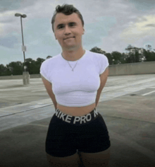 a man wearing a white crop top and black nike pro shorts stands in a parking lot