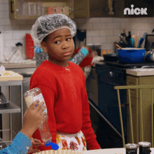 a boy wearing a plastic cap is standing in a kitchen with a nick logo on the wall behind him