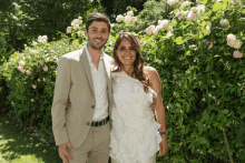 a man and woman posing for a picture in front of a bush