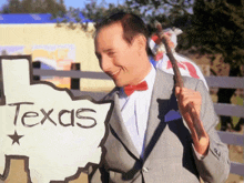 a man in a suit and bow tie holds a texas sign