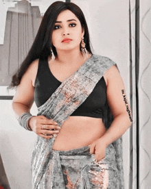 a woman is wearing a saree and a black crop top .