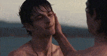 a man without a shirt is being touched by another man on the beach .
