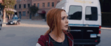 a woman with red hair is walking down a street next to a white van .