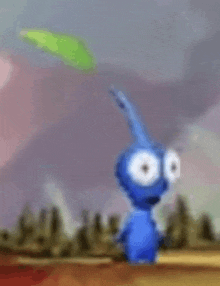 a blue cartoon character with big eyes is holding a green leaf in his hand .