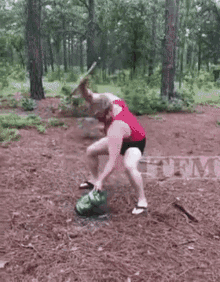 a man in a red shirt is kneeling down next to a watermelon with smoke coming out of it .