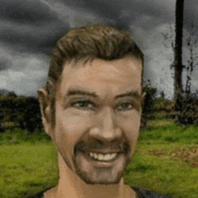 a man with a beard is smiling in a field with a storm in the background .