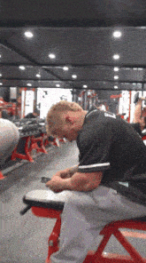 a man sitting on a bench in a gym wearing a black shirt with the number 9 on the back