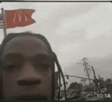 a man with dreadlocks is taking a selfie with a red flag flying in the background .