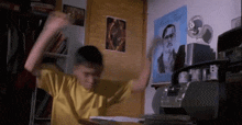 a young boy in a yellow shirt is sitting at a desk in a room with a poster on the wall .