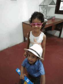 a little girl wearing pink sunglasses stands next to a little boy wearing a hat