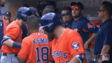 a group of baseball players are standing in a dugout and one of them is wearing a jersey with the number 18 on it .