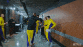 a group of men in yellow and purple uniforms are walking down a hallway with a netflix logo in the corner