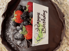 a chocolate cake with strawberries blackberries and blueberries and a happy birthday sign