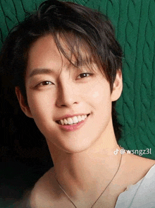 a young man wearing a white shirt and a necklace smiles