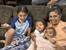 a woman sits on a couch with three children one of whom is wearing a shirt that says aloha