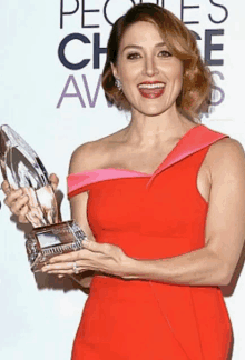 a woman in a red dress holds a trophy in front of a sign that says people 's choice awards