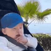 a baby is sitting in a stroller wearing a blue hat .