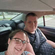 a man and a woman sit in the back seat of a car smiling