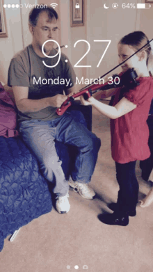 a phone screen shows a man and a girl playing violins on monday march 30