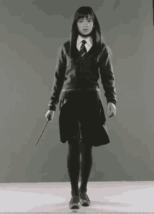 a girl in a school uniform holds a wand in her hand