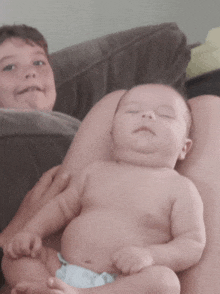 a baby in a diaper is laying on a woman 's lap next to a young boy