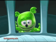 a green gummy bear is peeking out of a window and smiling .