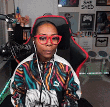 a woman wearing glasses is sitting in a chair with a sign that says she shed on the wall behind her