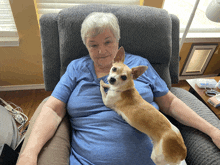 a woman in a blue shirt is sitting in a chair with a small dog on her lap