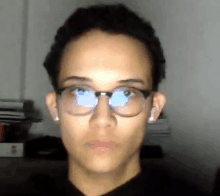 a young man wearing glasses and ear buds looks at the camera .