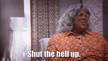 a woman in a floral dress is sitting in a chair and saying shut the hell up .