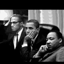 a black and white photo of three men sitting next to each other in suits and ties .