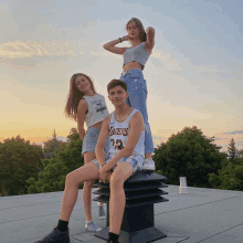 a man wearing a lakers jersey sits on a roof with two women