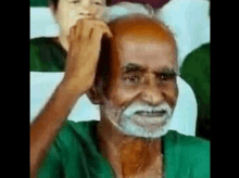 a man with a beard and a green shirt is smiling while holding his head .