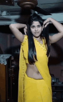 a woman in a yellow saree is adjusting her hair