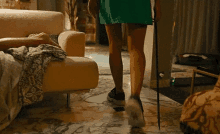 a woman in a green dress is walking with a cane in a living room next to a couch .