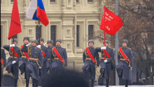 a group of soldiers marching in front of a building with a red flag that says ' a ' on it