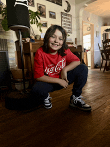 a boy wearing a red coca cola shirt is squatting on the floor