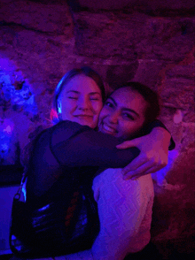 two women are hugging each other in a dark room with purple lights